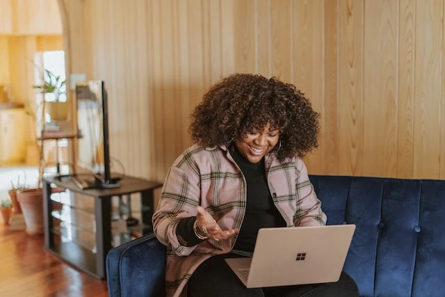 Smiling property manager sitting on a blue velvet couch using their laptop