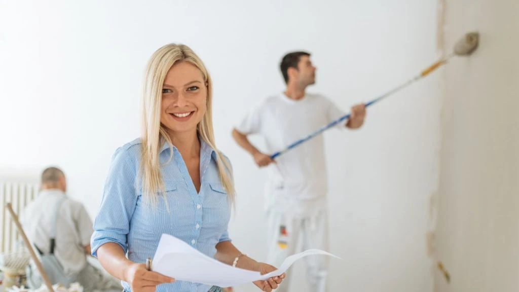 Smiling person standing in front of two people painting a room