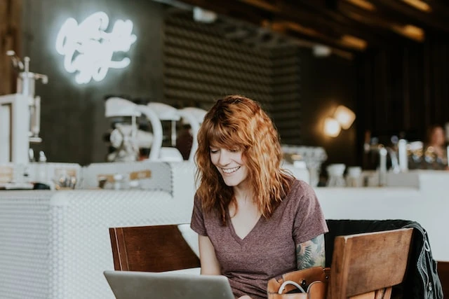 Smiling person with red hair sitting in a cafe and working on a laptop to research fair market rent