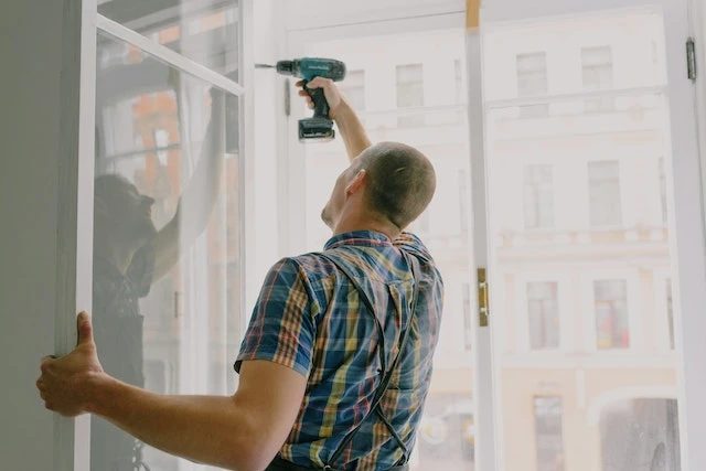 someone-in-a-plaid-shirt-using-a-drill-to-fix-a-window