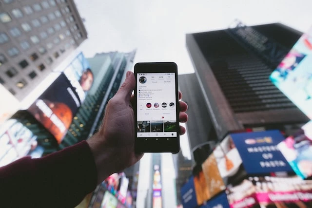 Someone’s hand holding up a phone in front of buildings and billboards