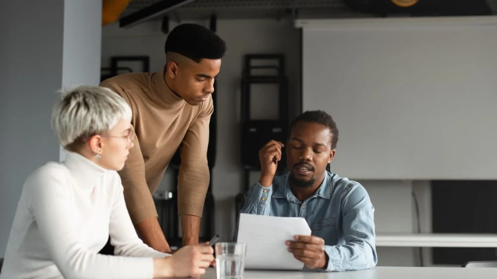 One person leaning on a table while two other property managers look at a document about security deposits together property management companies