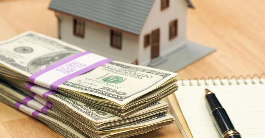 three stacks of cash in front of a small house