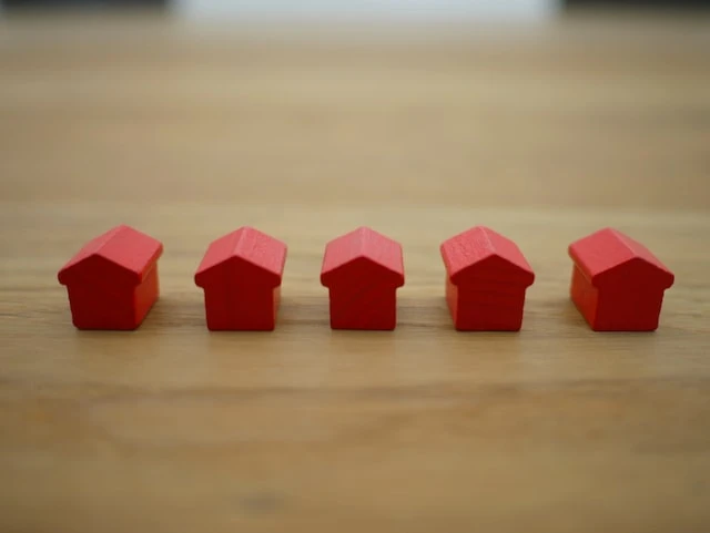 Five red Monopoly houses lined up on a wooden table