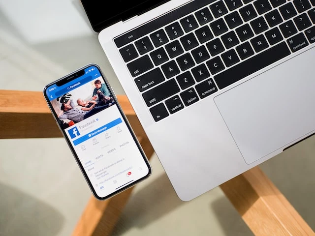 A smartphone open to the Facebook app next to an open laptop keyboard