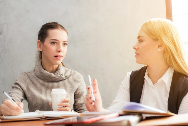 Two landlords sitting at a table having a discussion with notebooks and coffee cups