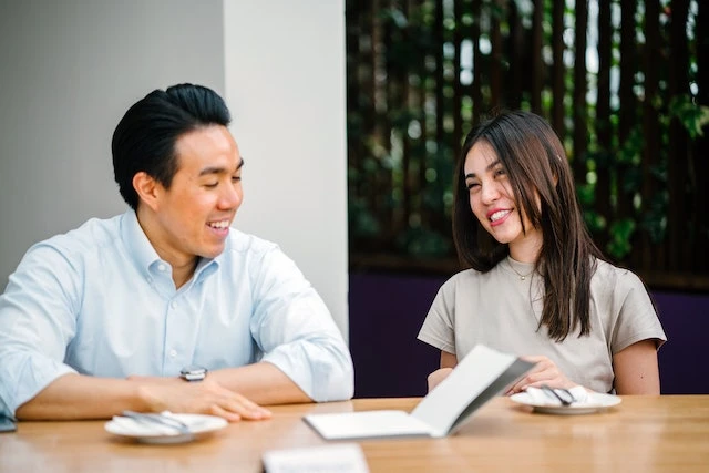 Two people sitting at a wooden table smiling and talking