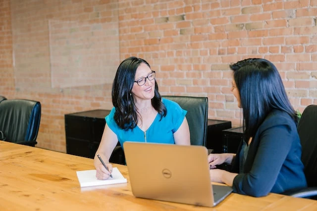 A property manager and her client sitting on the same side of a table talking about something on the open laptop in front of them
