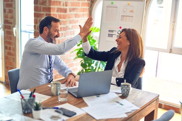 Two people working at a table together, they are high fiving