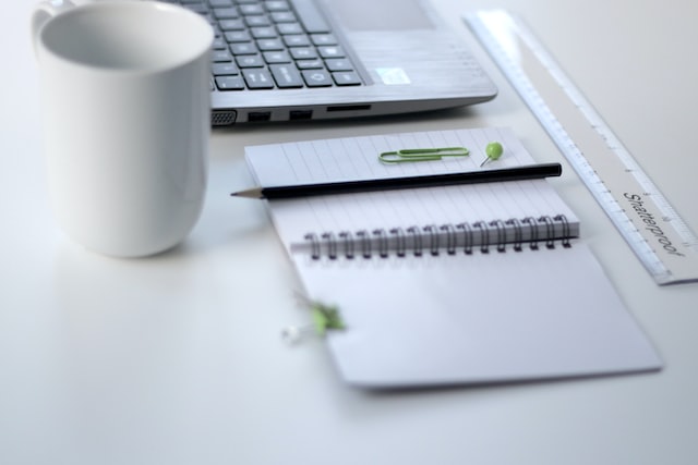 A desk set up with a notebook, keyboard, pens, and coffee mug