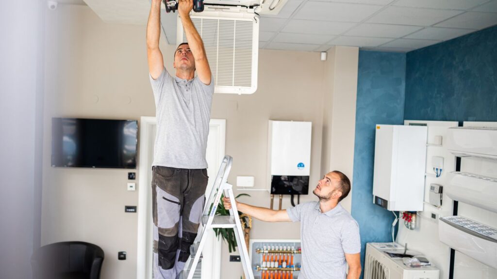 Two people fixing an AC unit in a ceiling