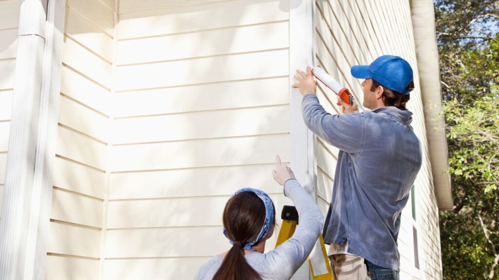 Two people working on the side of a house