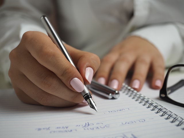 Property managers hands with pink nail polish using a fountain pen to write notes