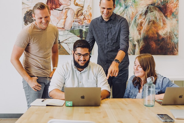 Four people working on a laptop around a table, two are seated and two are standing