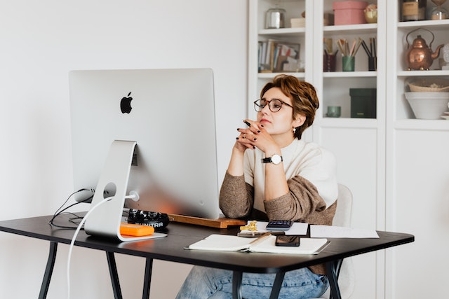 Person sitting at their desk looking thoughtfully at their desktop computer screen