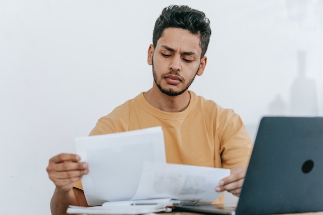 Person looking at papers at a desk in front of a laptop
