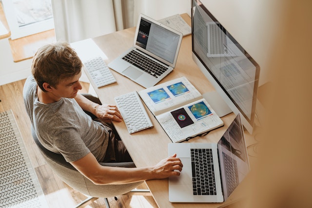 Person working at a desk with two laptops and a desktop