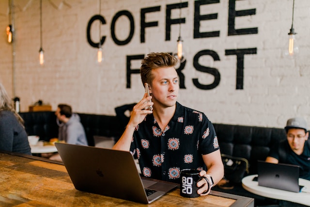 Person in a coffee shop working on a laptop while talking on the phone