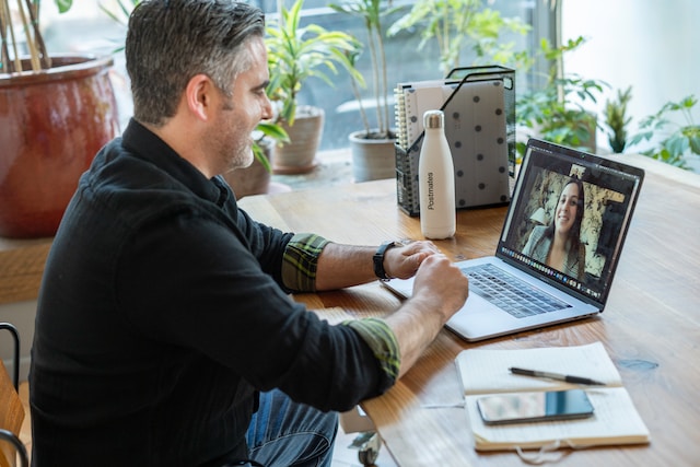 A person sitting at a desk in front of a laptop having a video call with another person