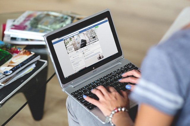 person in a white long-sleeve shirt using a macbook air to make a facebook post