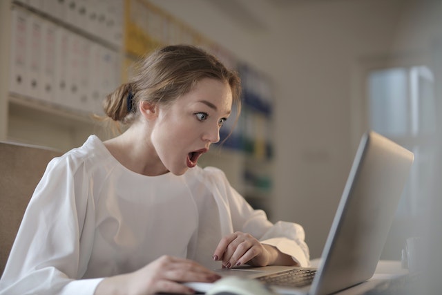 Woman in a white top looking shocked at something on her laptop in front of her