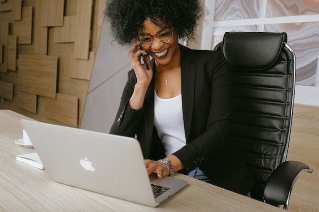 Smiling woman talking on the phone and also working on her laptop