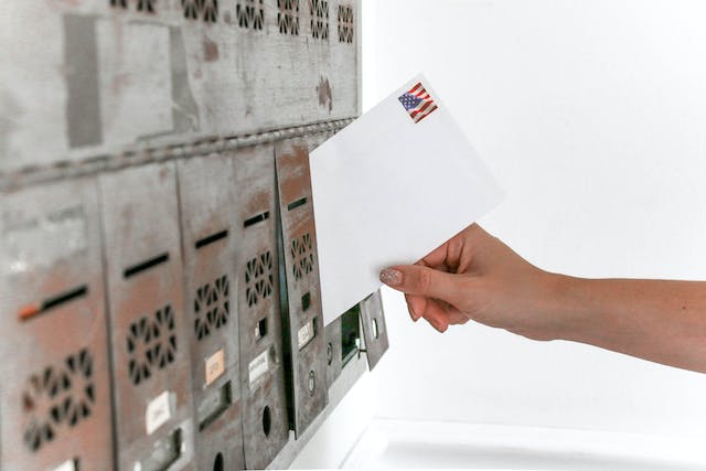 A person's hand placing a letter in a silver mailbox