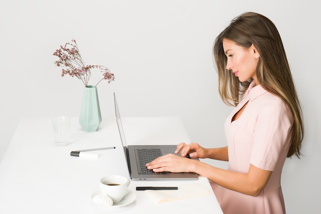 Woman in a pink dress working on her laptop at a white table