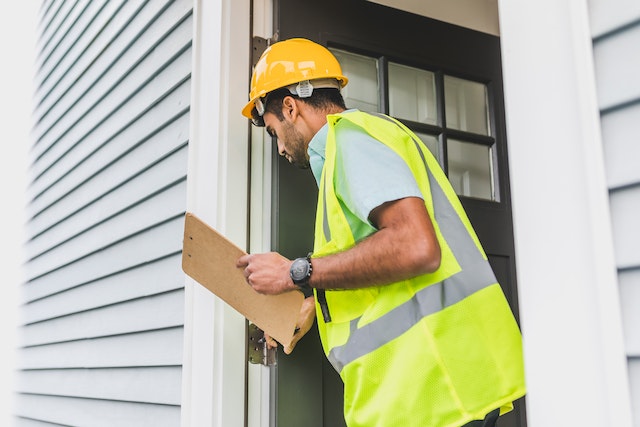 Inspector in a yellow high-visibility vest and hard hat approaching a door while holding a clipboard