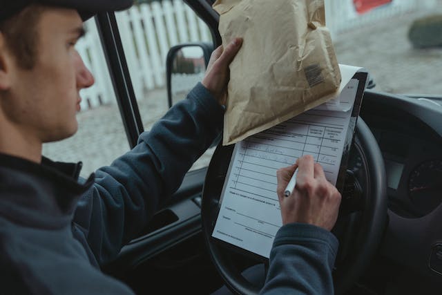 Mail delivery person in their truck writing on a delivery slip
