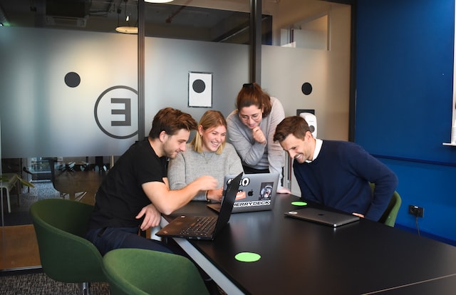 Four people crowded around a laptop in an office