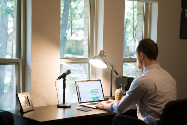 Person sitting at a desk in fron of a window working on a laptop