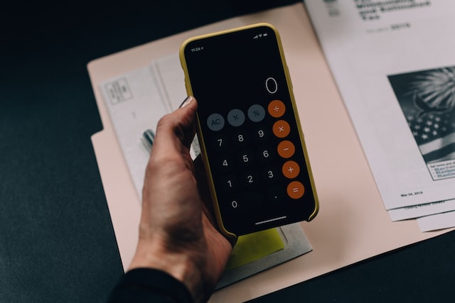 Person's hand holding a phone open to the calculator app over an open file folder
