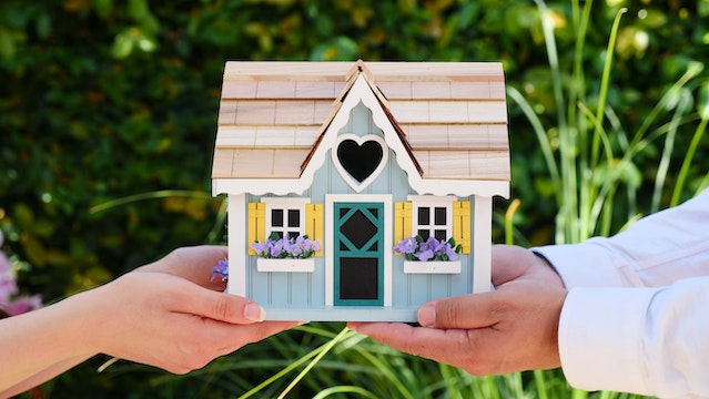 Two people’s hands holding a miniature house