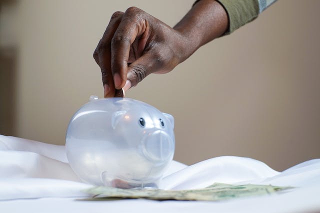 Hand placing a coin in a transparent piggy bank, as a security deposit