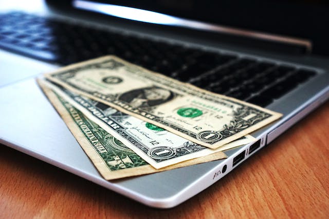Three one dollar bills on the edge of an open laptop, money paid