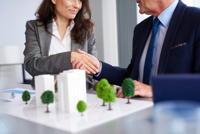 Two professionals shaking hands over a small diagram of a building development
