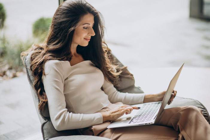 Relaxed woman with long brown hair sitting in an armchair and working on her laptop