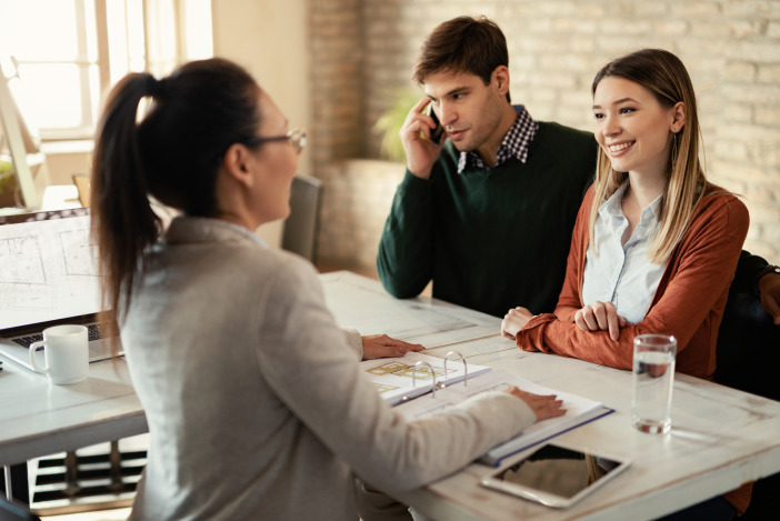 A property manager sitting on one side of a desk speaking to a man and a woman across from her, the man is on the phone