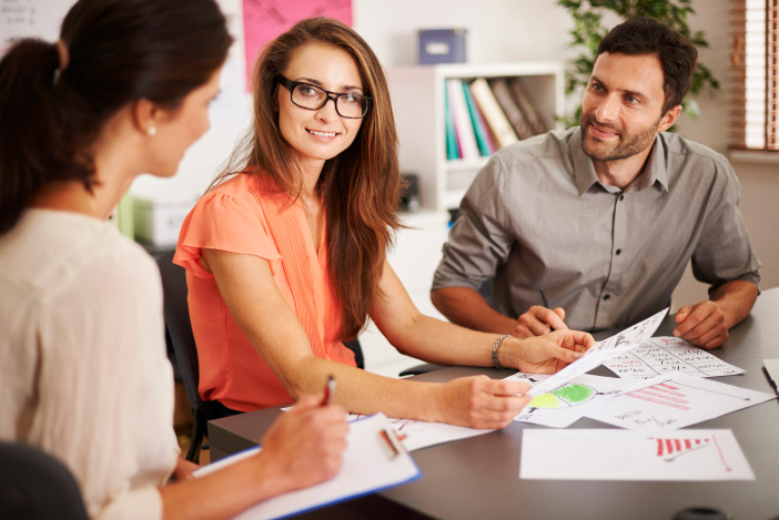 Three people working at a table together, reviewing the documents in front of them