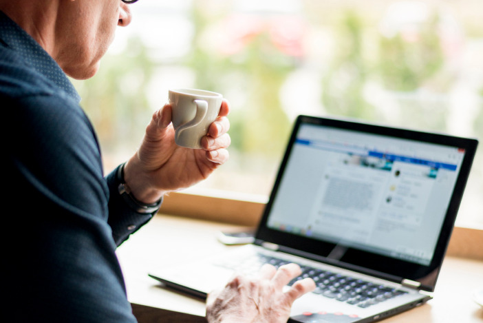 Person drinking a coffee and looking at LinkedIn on the laptop in front of them