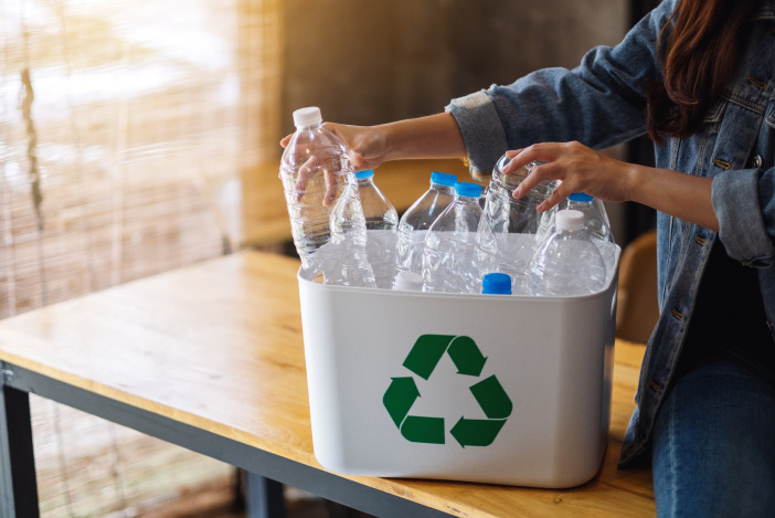 A person placing plastic bottles in a white recycling bin with a green recycling symbol on the front