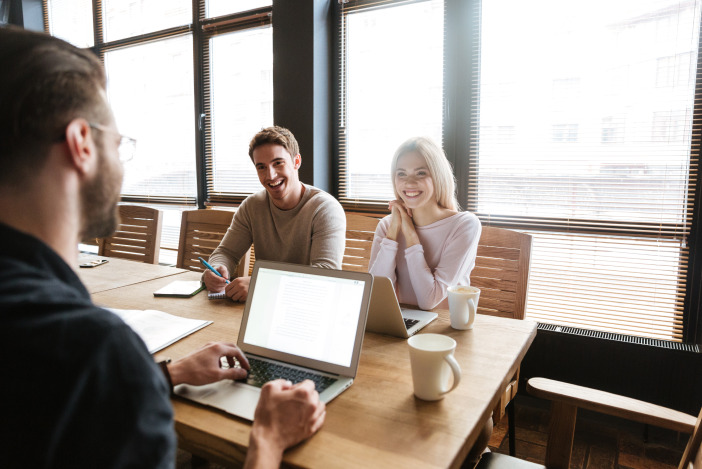 Two people sitting across a desk from another person looking at their laptop