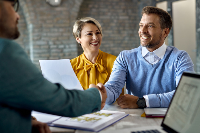 A smiling man and woman sitting across a desk from their property manager, the man is shaking the property manager's hand