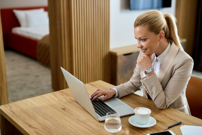 Smiling blonde woman working at a desk with a cappuccino and a laptop