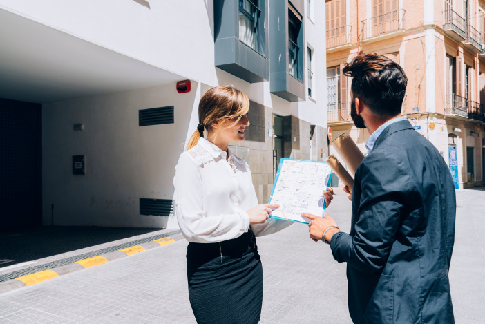 Two people in professional dress standing outside looking over a document together