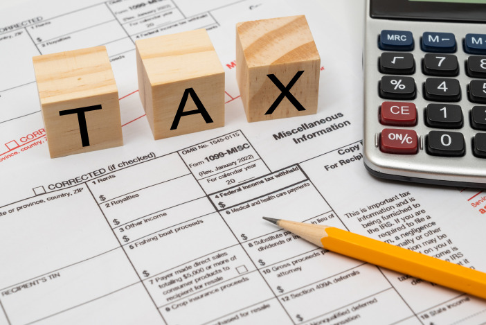 Tax documents with a pencil, calculator, and three wood blocks spelling out "TAX"